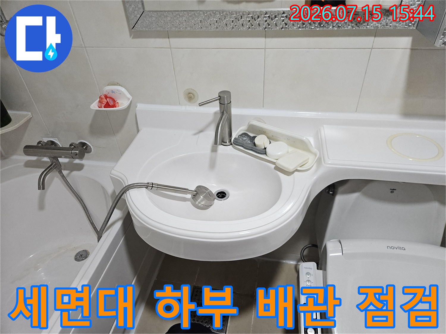 흰색 세면대 아래쪽으로 노출된 수전과 배관 연결 부위를 점검하는 모습