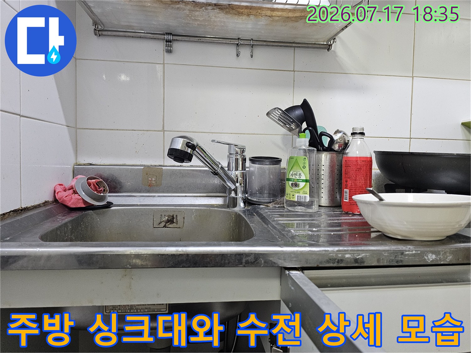 금속제 싱크대 볼 위에 설치된 주방 수전과 그 옆의 세척 도구들