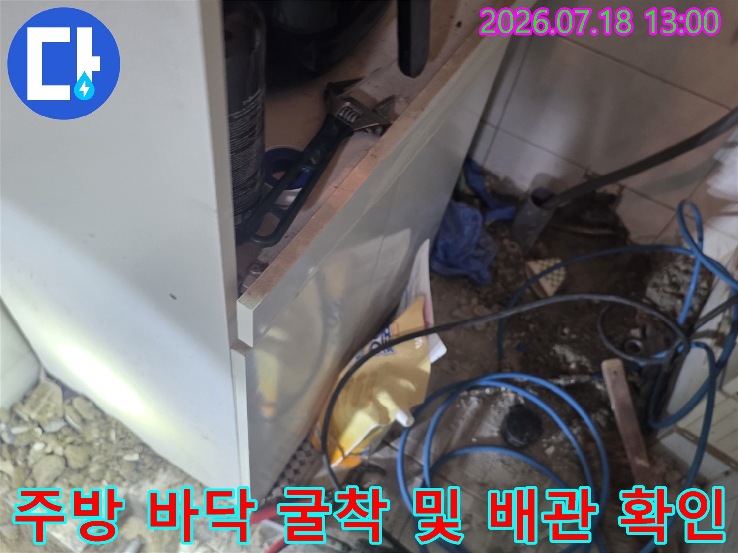 싱크대 하단 바닥 타일을 제거하고 파란색 배관과 탐지 장비를 배치한 현장 사진