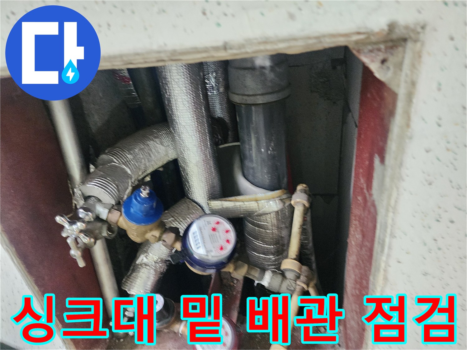 보온재가 입혀진 배관과 계량기가 있는 싱크대 하부 내부 모습입니다.