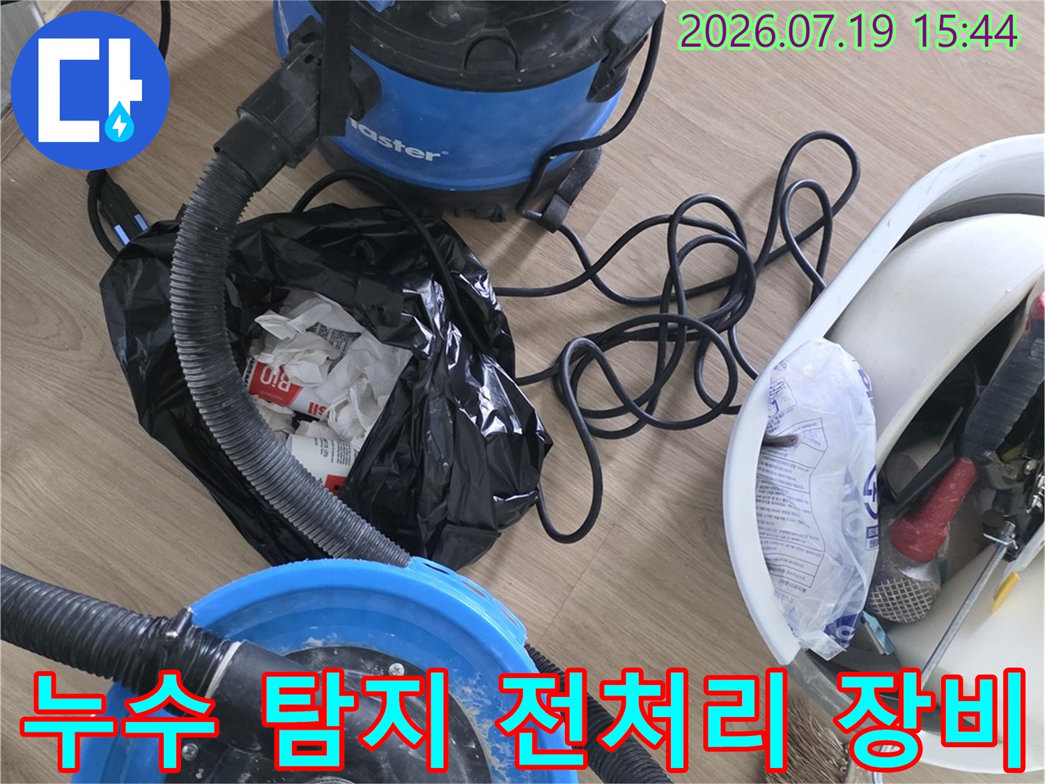 파란색 진공 흡입기와 호스-도구함이 배치된 화장실 바닥 작업 모습