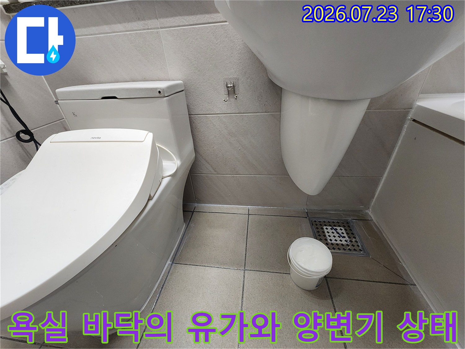 밝은 색상의 욕실 타일 위에 배치된 변기와 금속제 사각 배수구-유가