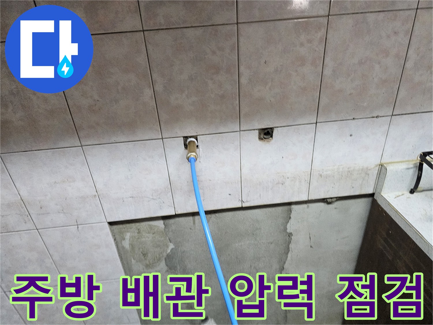 주방 타일 벽면의 수도 연결 부위와 파란색 호스 점검 상태
