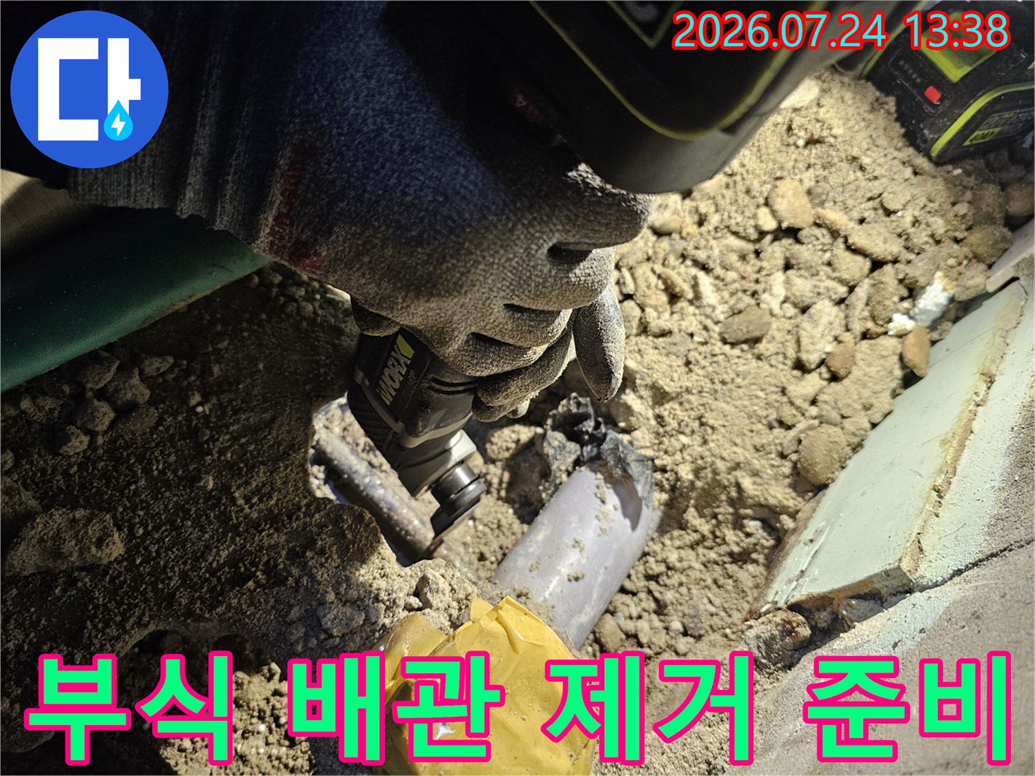 흙과 자갈이 섞인 바닥면에서 노출된 부식된 파이프와 작업 도구-장갑 사진