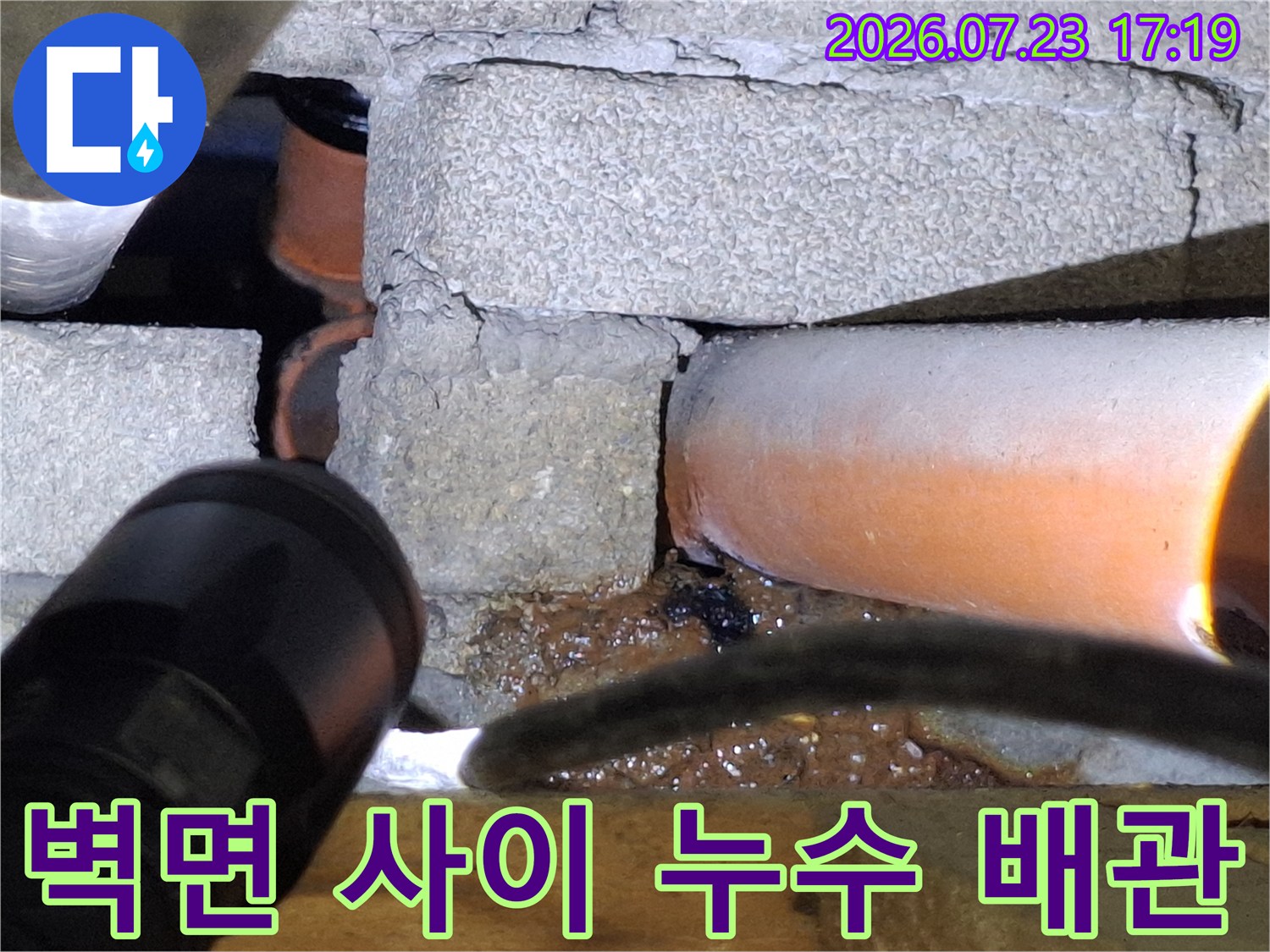 어두운 공간에서 손전등 빛을 통해 오렌지색 배관의 누수 부위를 비추는 장면