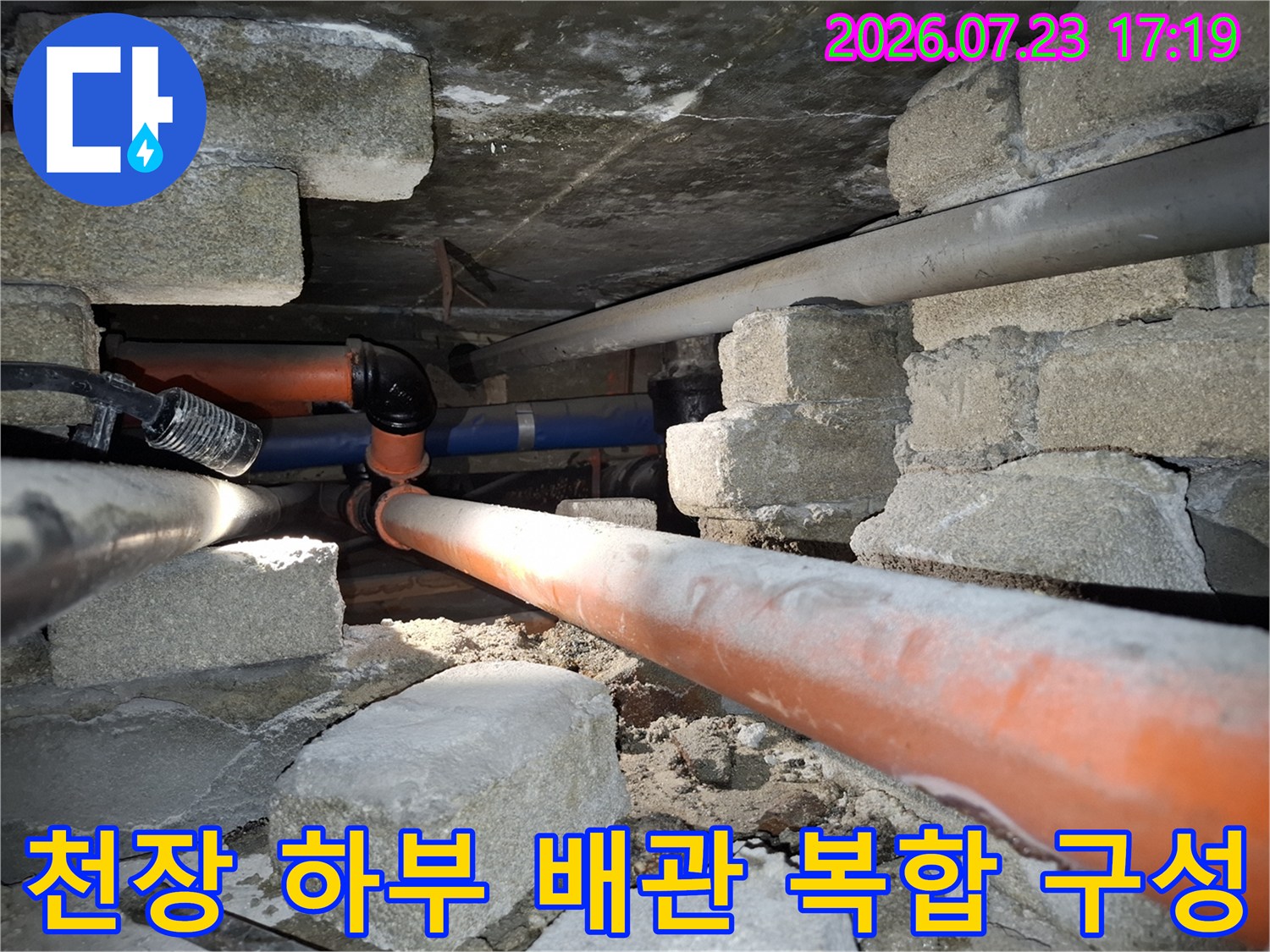 오렌지색 PVC 관과 파란색 배관이 교차하여 설치된 건물 내부의 하부 구조-배관 점검 중