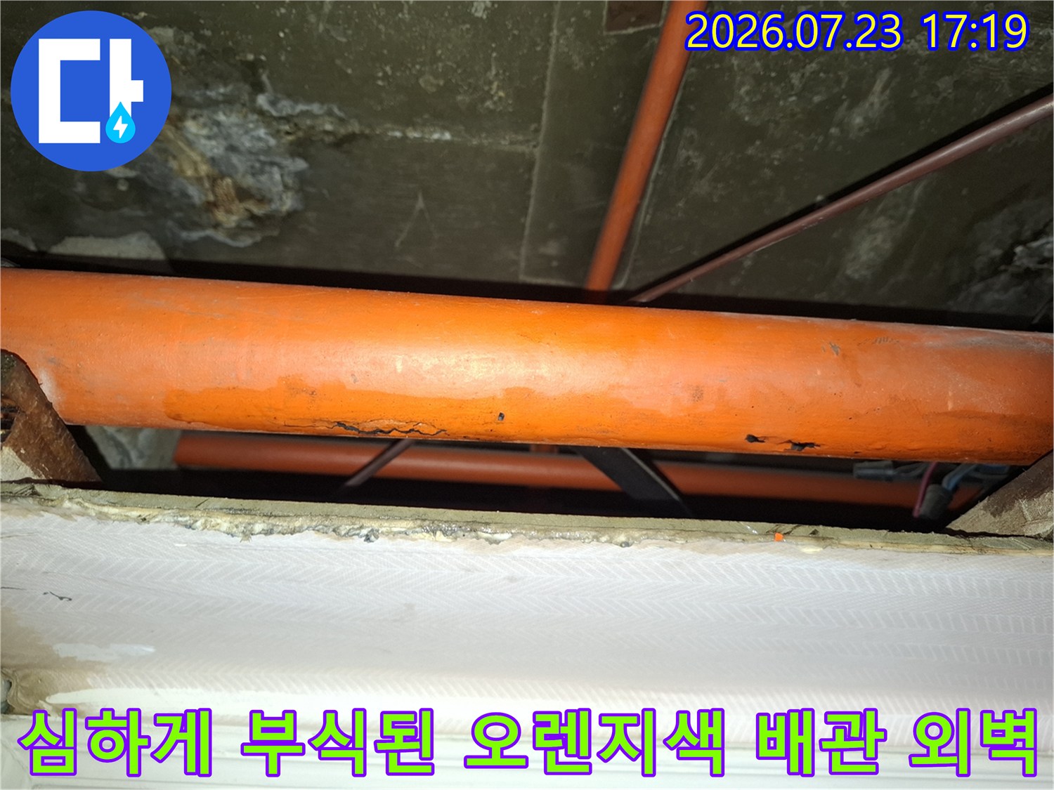표면이 거칠게 부식되어 누수가 발생한 천장 내부의 오렌지색 배관 모습