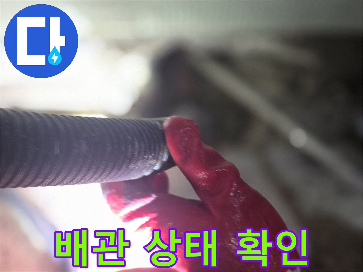 검은색 주름관 배관을 작업자가 붉은 장갑으로 잡고 검사하고 있습니다.
