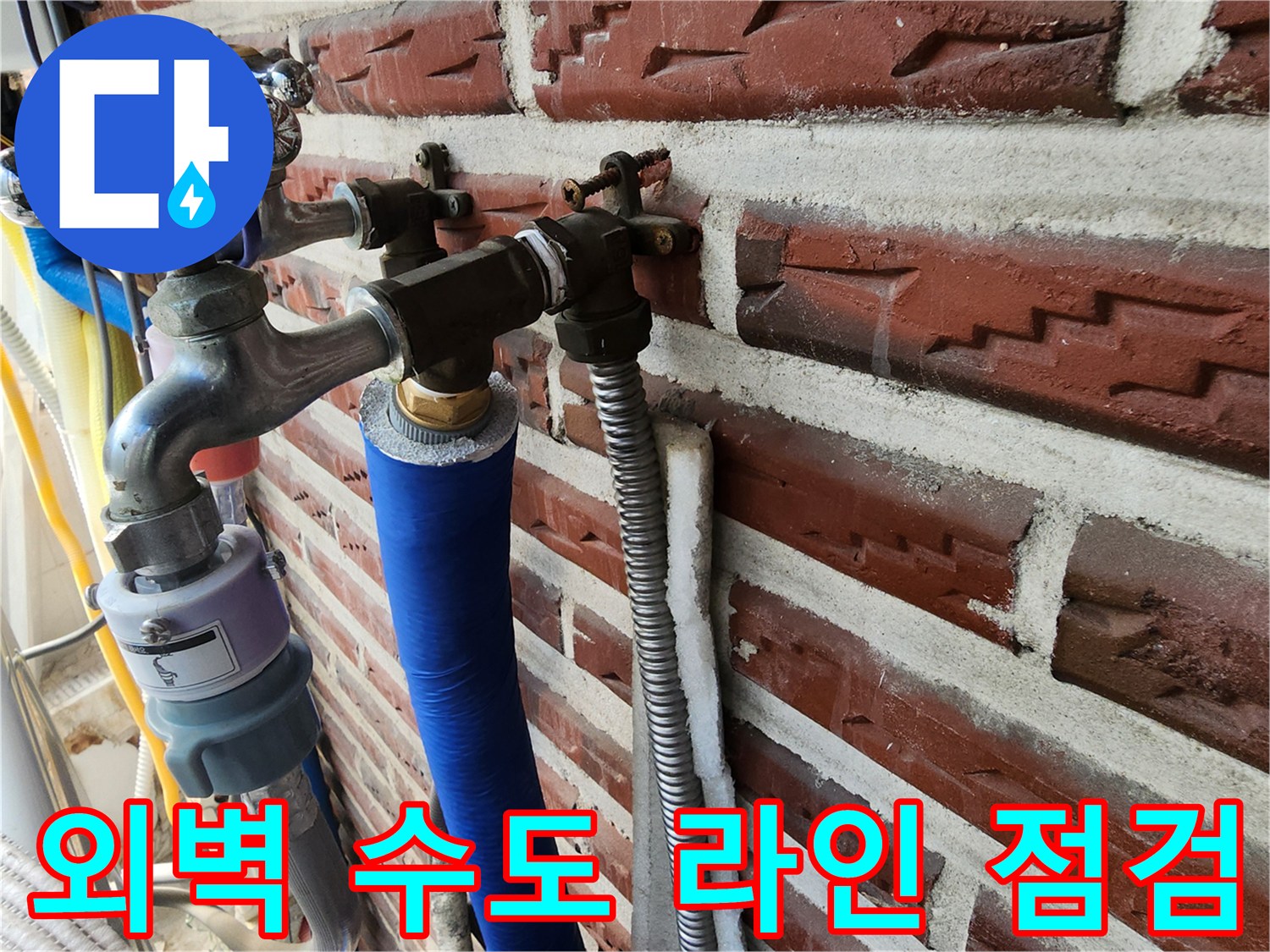 벽돌 외벽에 설치된 금속 배관과 파란색 보온재가 씌워진 호스입니다.