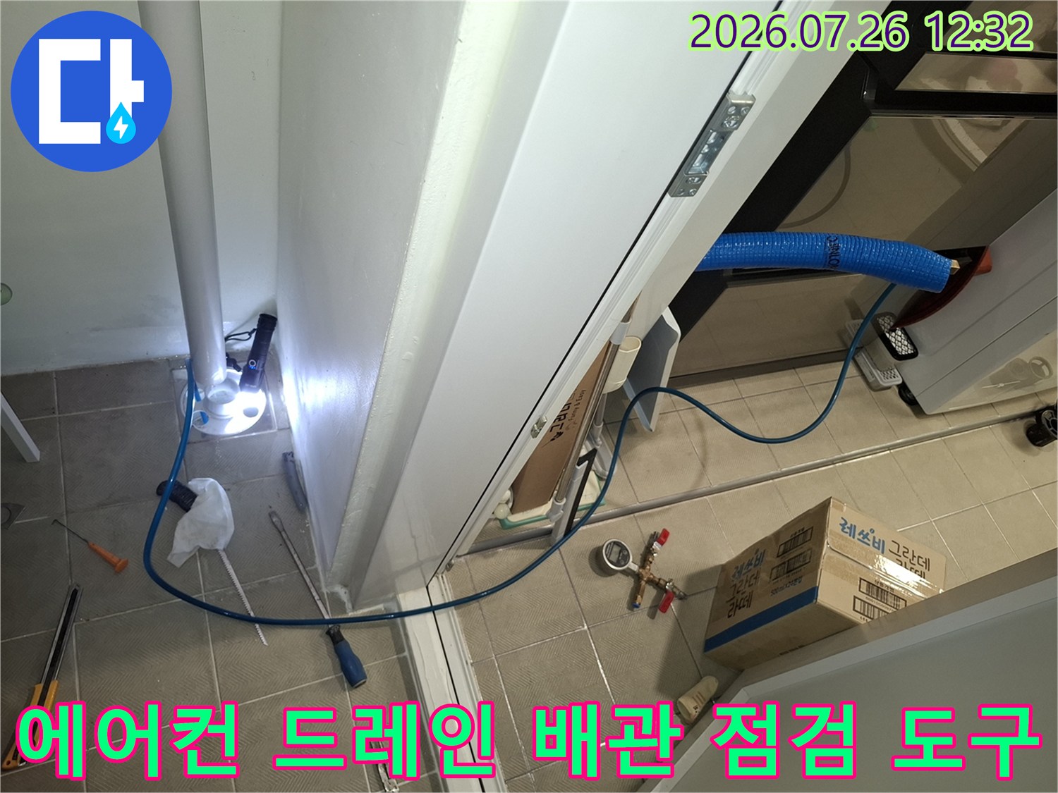 흰색 벽면과 바닥 타일 사이에 설치된 파란색 에어컨 배관-작업용 렌치와 압력계