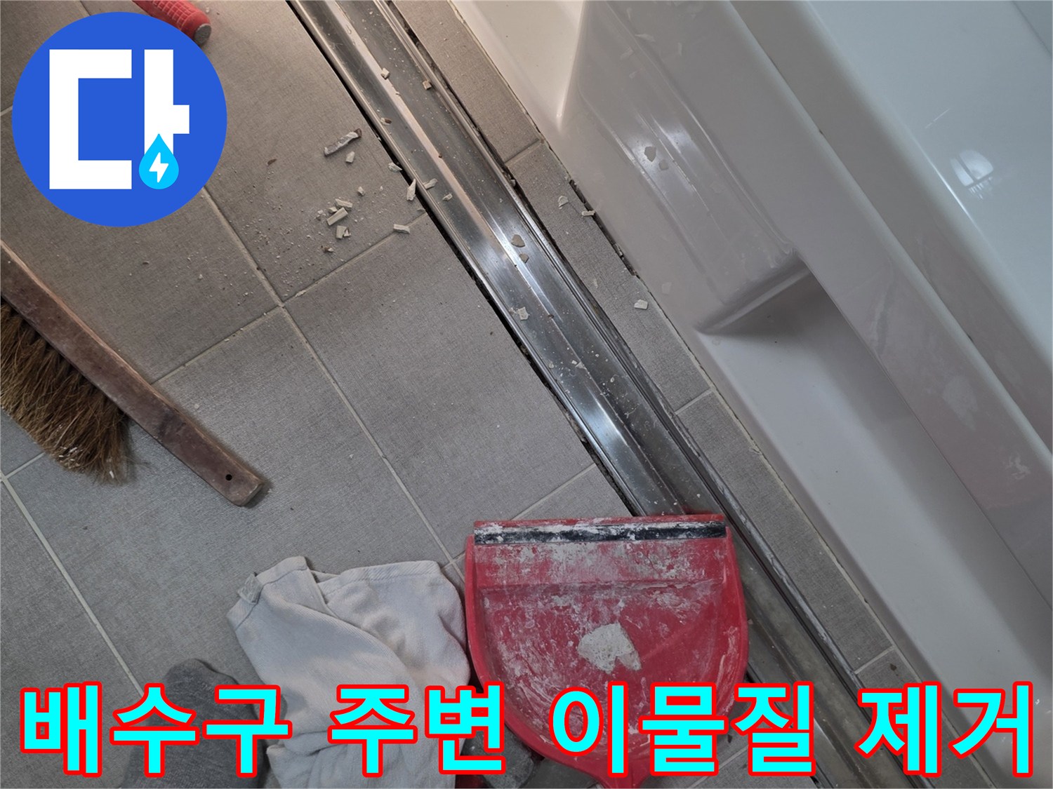 붉은색 쓰레받기와 청소 도구가 놓인 욕실 배수구 현장
