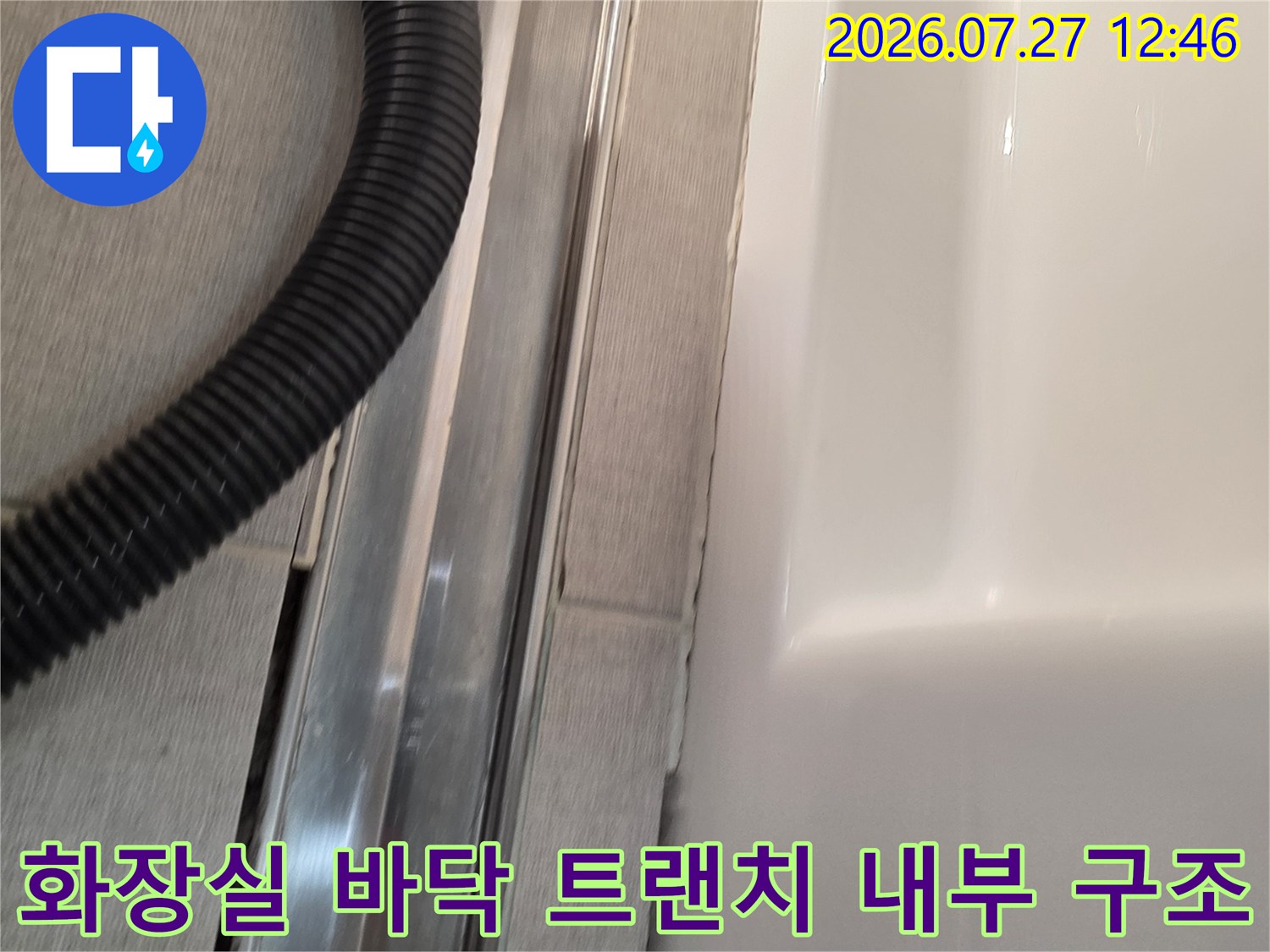 욕실 내 금속 배수구 트랜치가 열려 있고 검은색 석션 호스가 놓인 모습