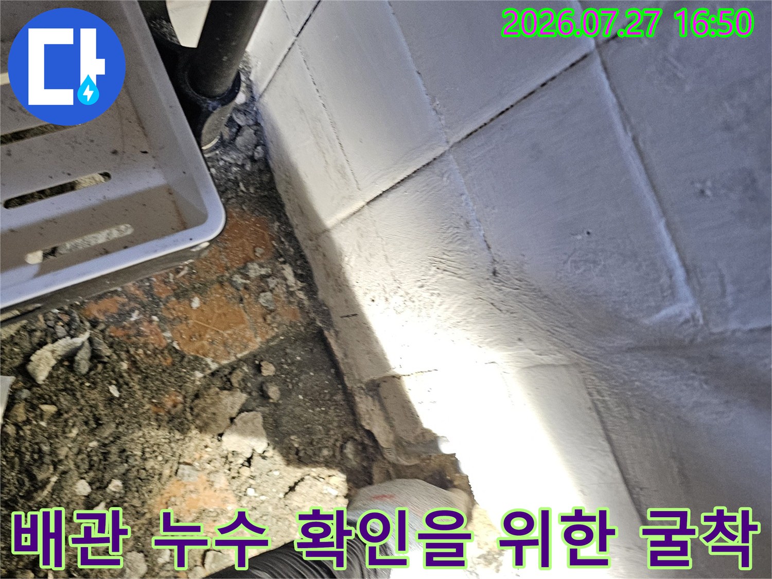 전문 장갑을 착용한 작업자가 화장실 바닥의 파헤쳐진 배관 부위를 점검하고 있는 사진