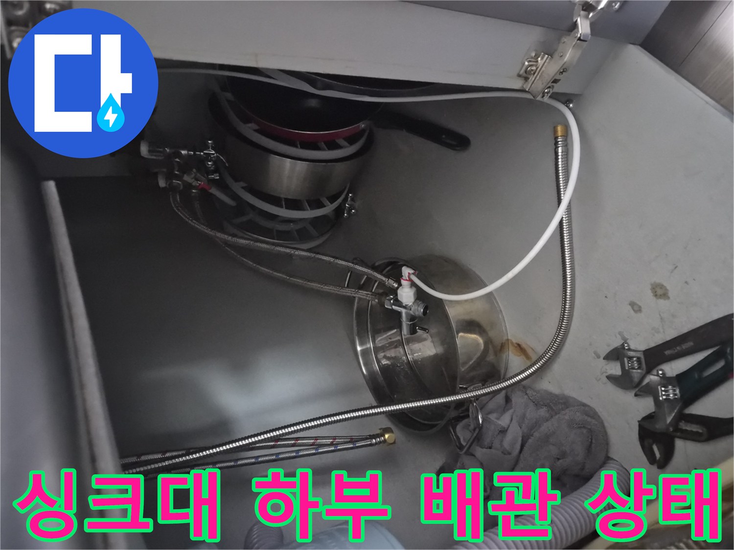 식기세척기 급수 호스와 연결 부속이 보이는 싱크대 내부 사진