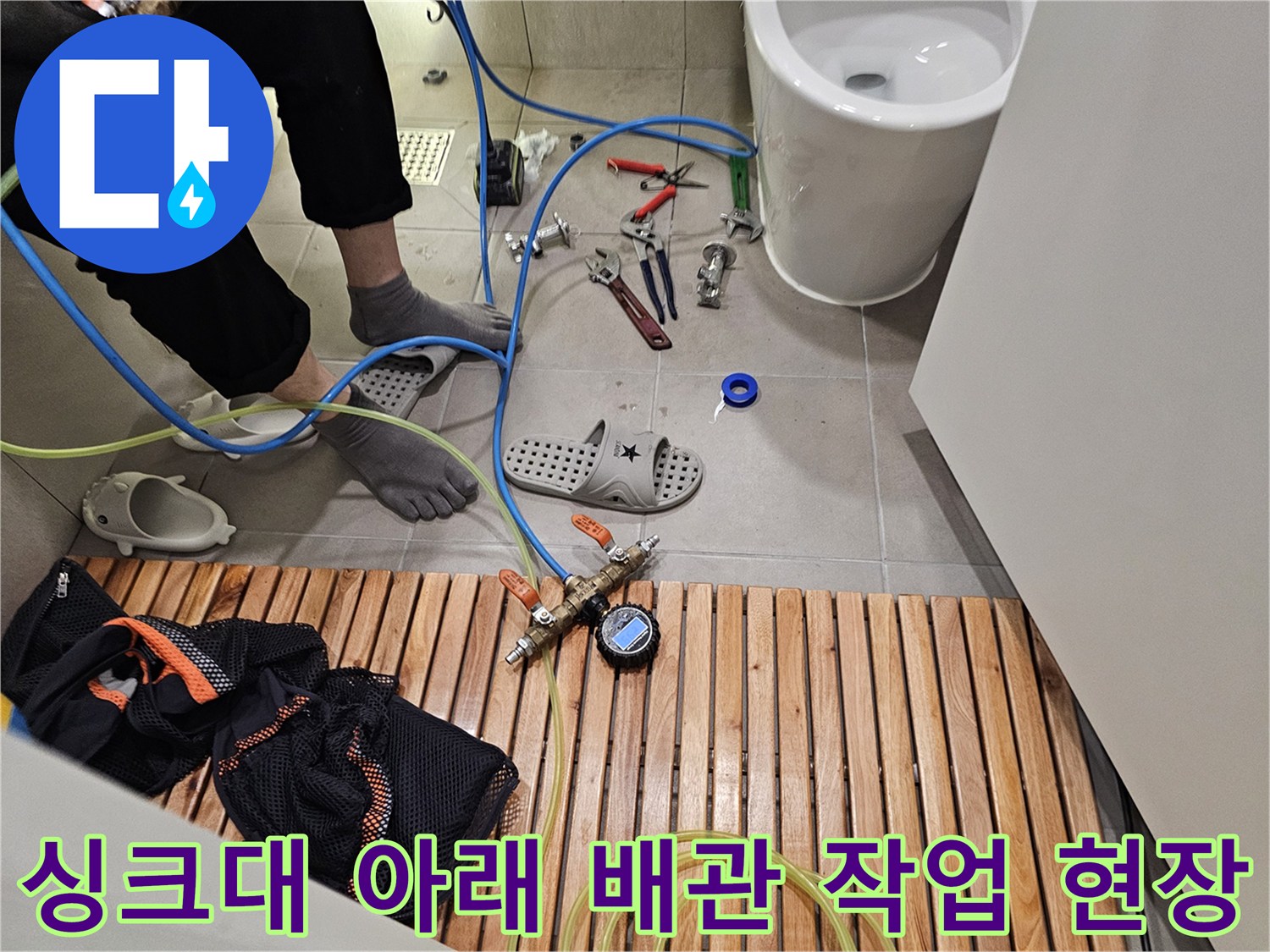 싱크대 하단 바닥에 배치된 배관 연결 부품과 수리용 공구들