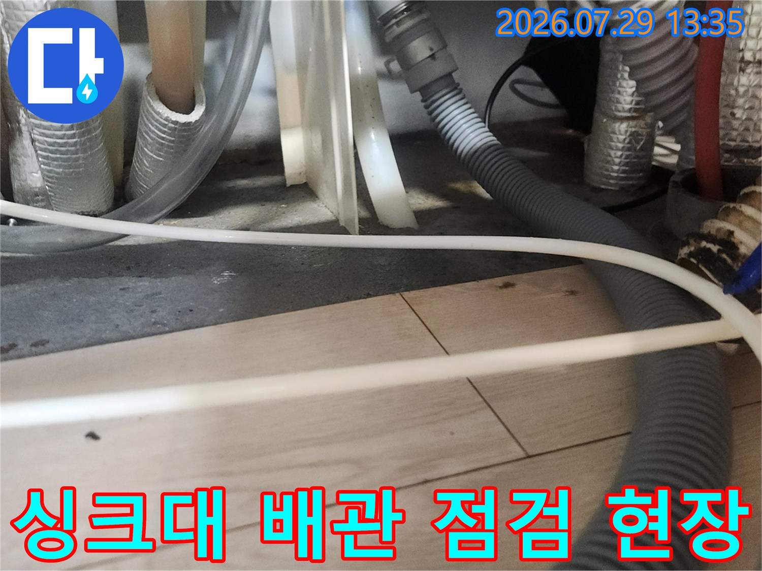 싱크대 하부의 노출된 배수관과 절연재로 감싸진 파이프라인 모습