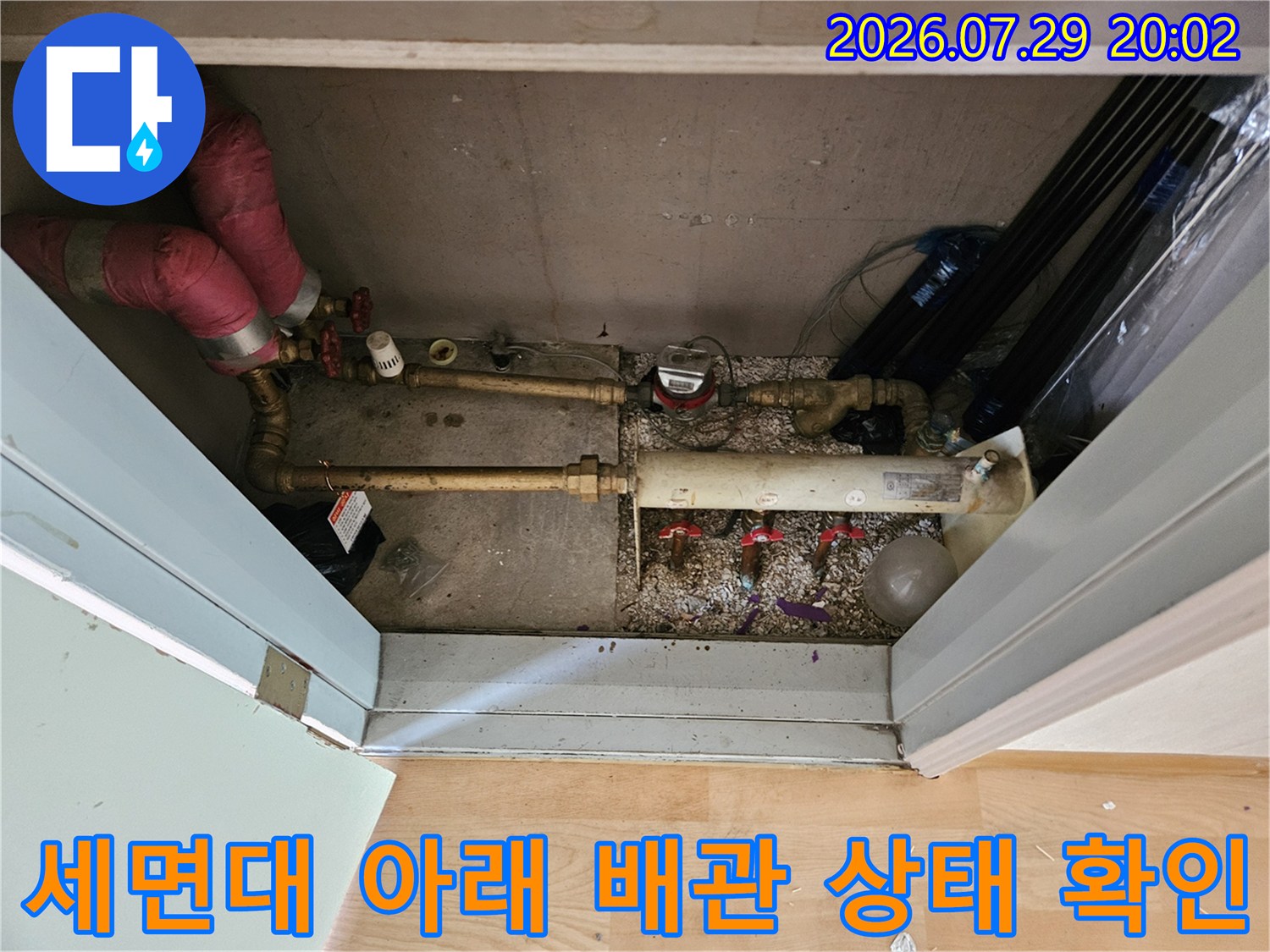 세면대 밑에 노출된 수많은 수도 배관들의 연결 부위와 전체적인 경로를 점검하는 모습