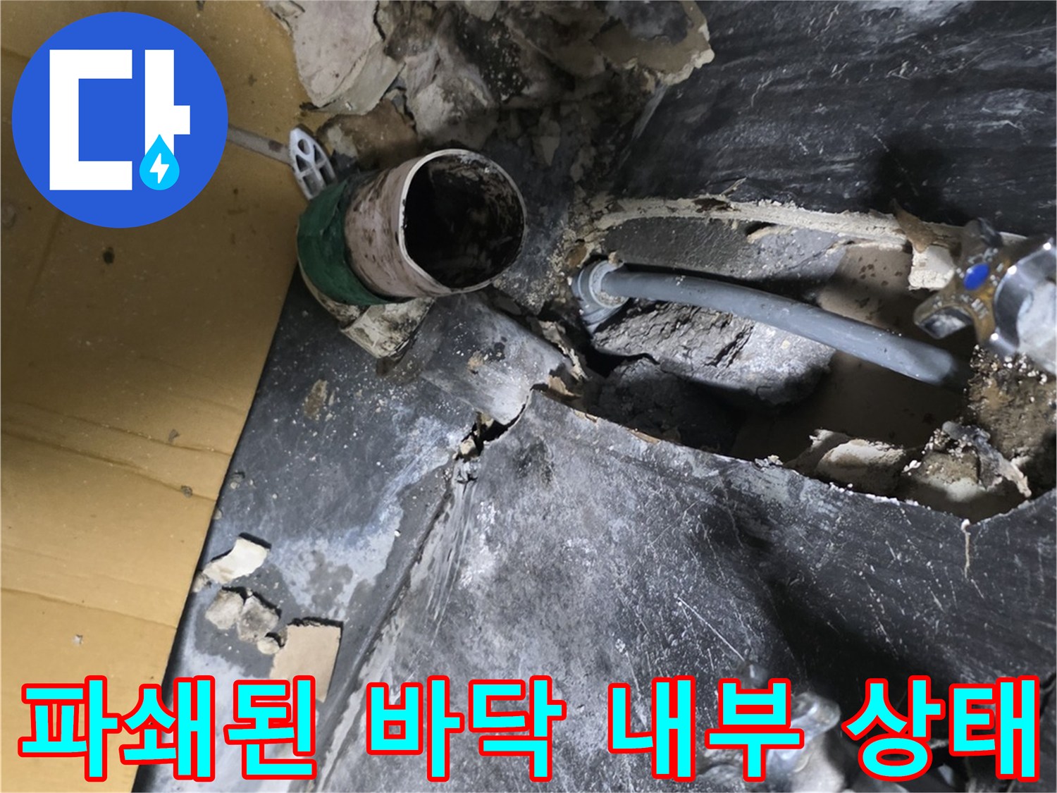 배관 주변의 파손된 마감재와 습기가 찬 바닥을 보여줍니다.