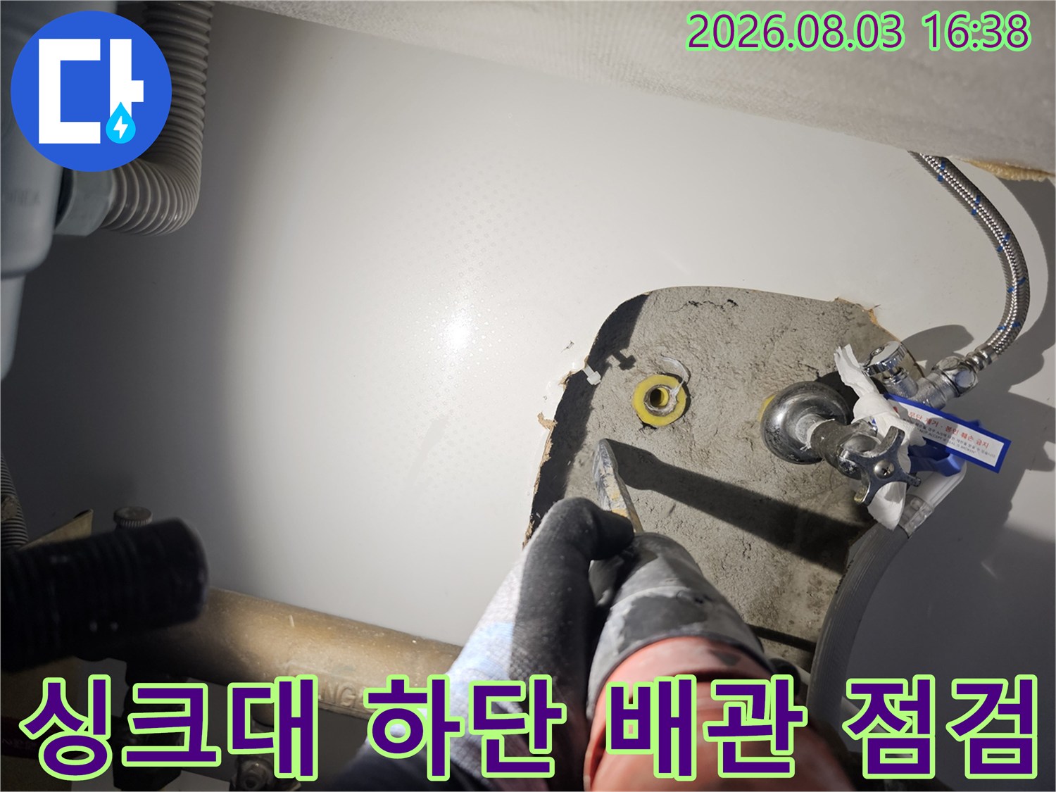 싱크대 하부의 노란색과 회색이 섞인 배관 부위를 작업자가 세밀하게 검사하는 모습