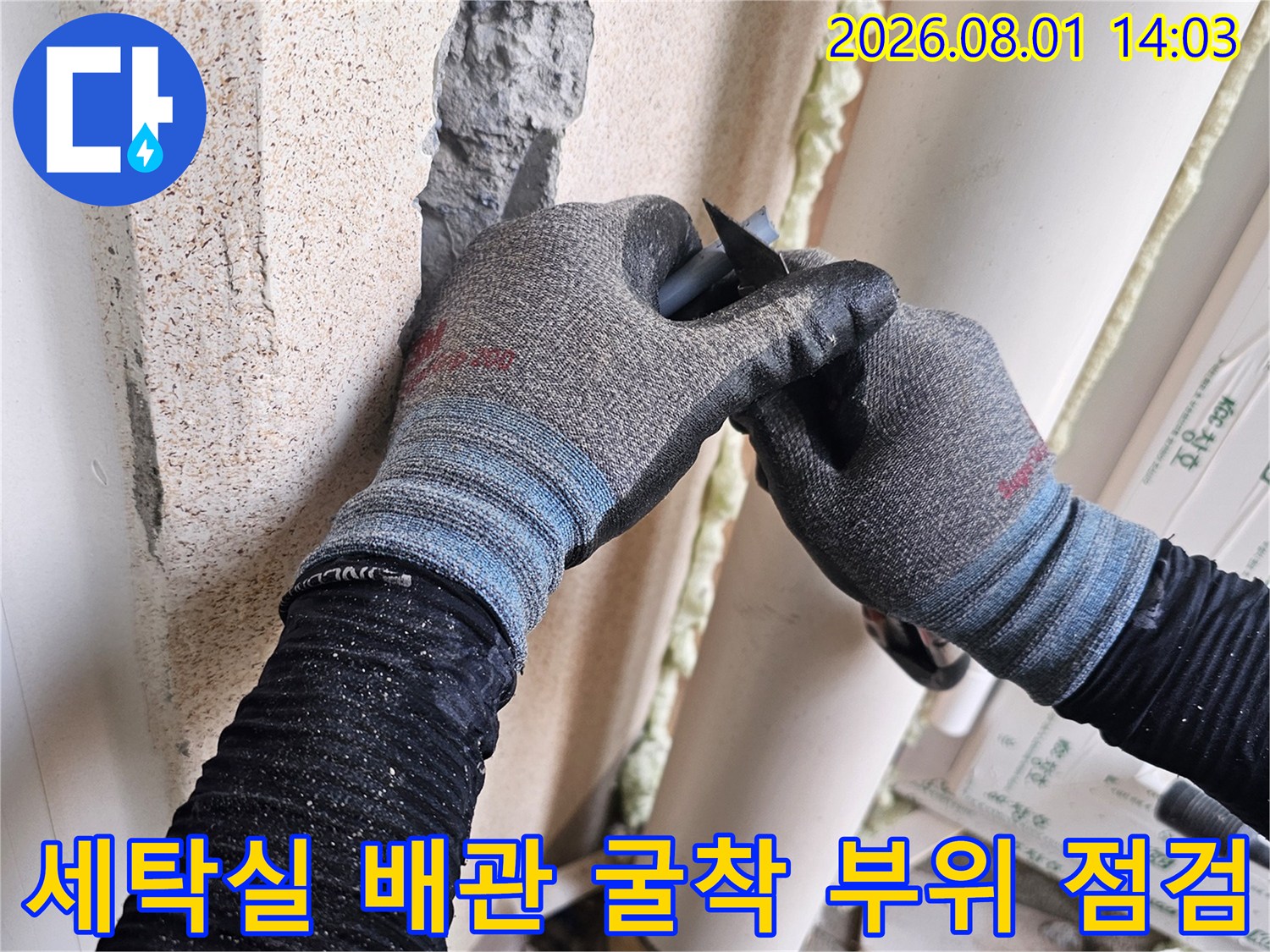 작업자가 장갑을 끼고 세탁실 벽면의 노출된 배관 파손 부위를 확인하는 모습