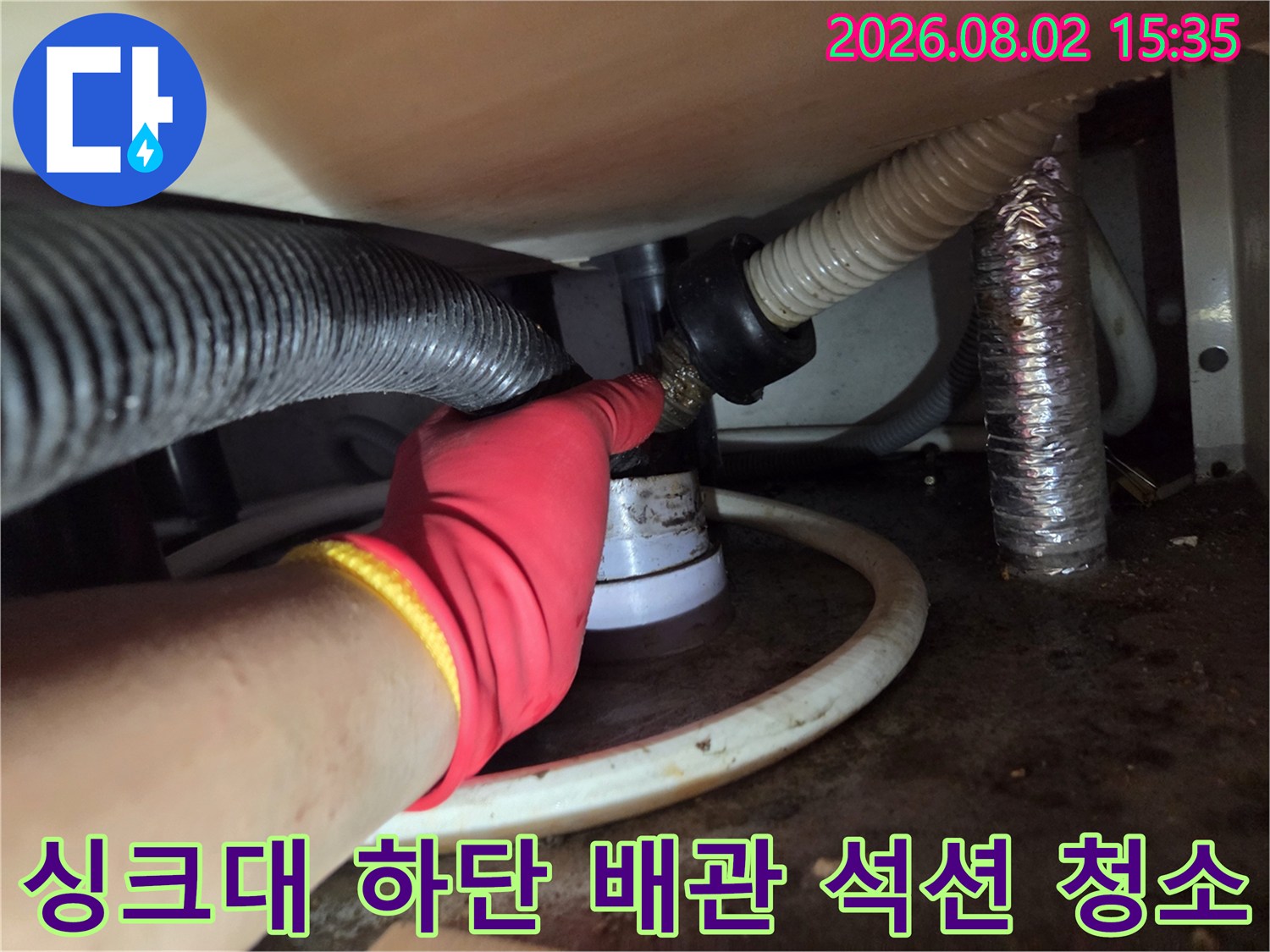 싱크대 아래 공간에서 석션 장비를 연결하여 막힌 배수 호스 내 이물질을 제거하는 장면