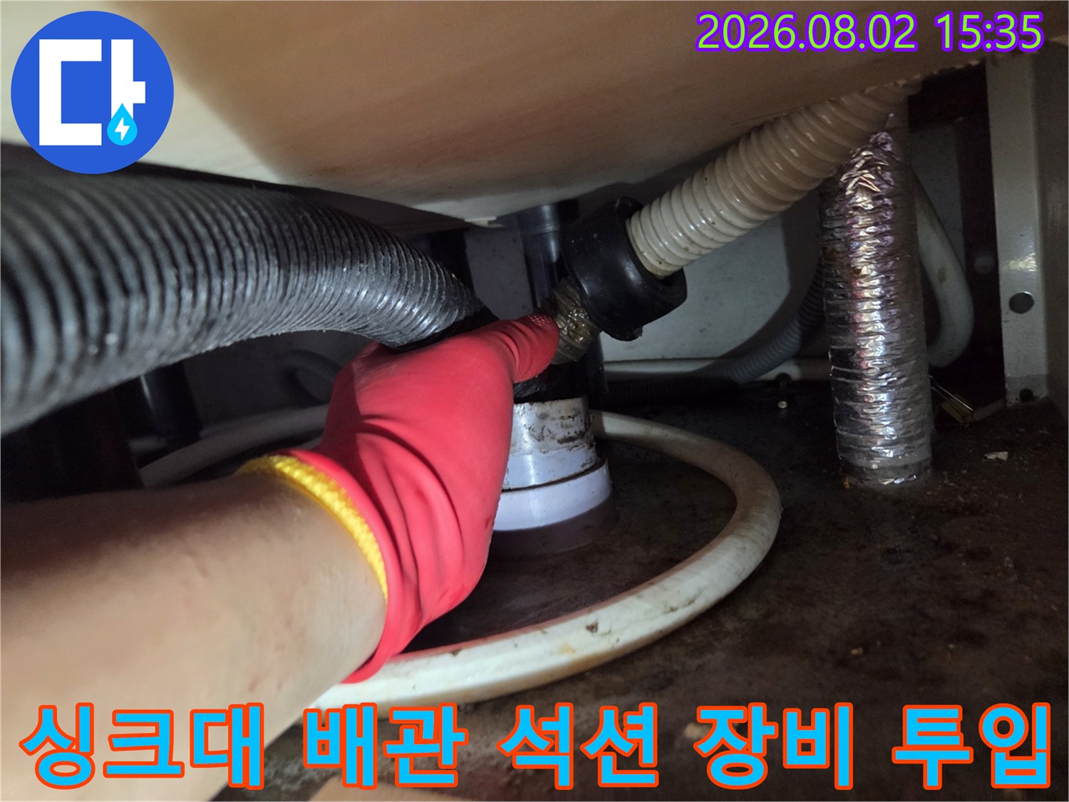 작업자가 싱크대 하단에 위치한 배수 굴곡부에 석션 장비를 연결하여 내부 이물질을 흡입하는 현장 사진.
