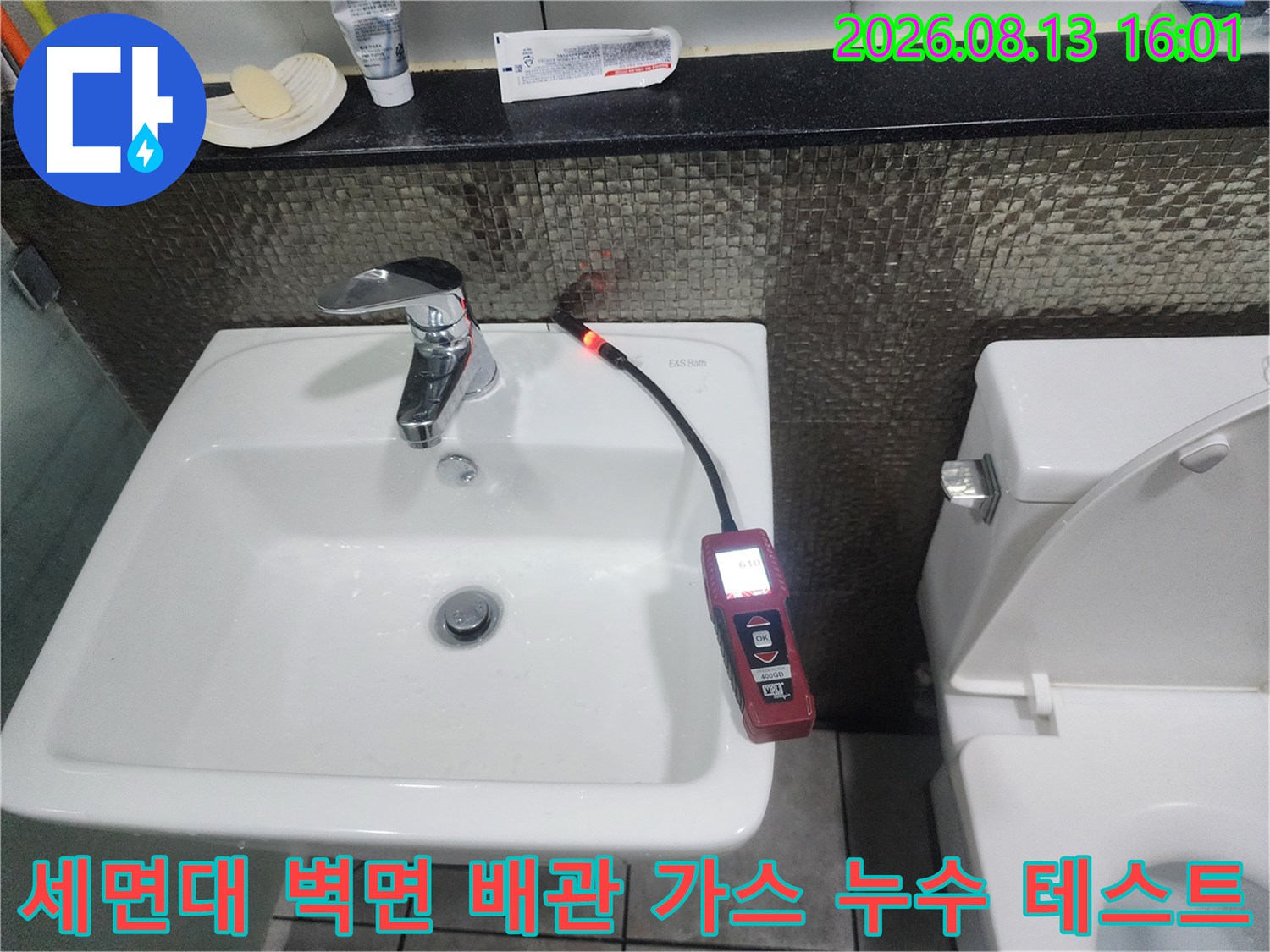 세면대 수전 근처 벽체 틈새로 가스 탐지 센서를 위치시켜 배관의 기밀 상태를 점검하는 모습입니다.
