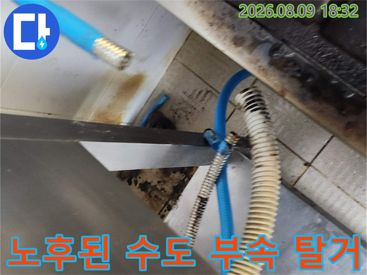 오염된 배관과 파란색 호스가 연결된 싱크대 하부의 작업 현장 모습입니다.