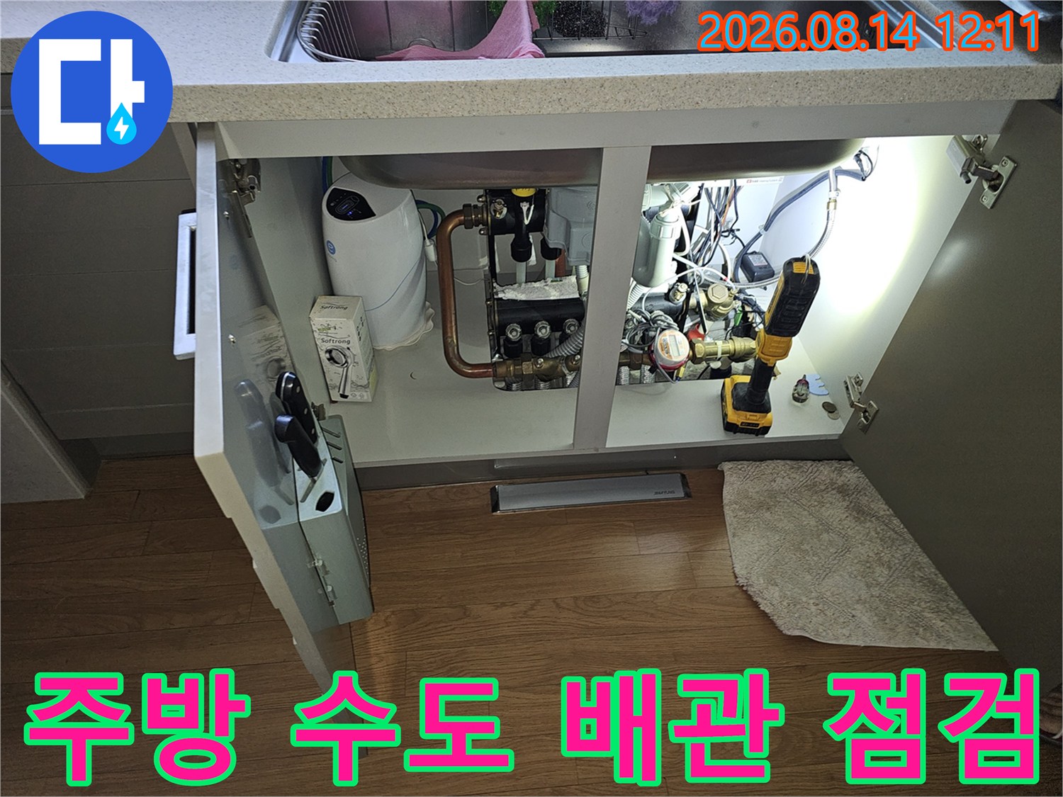싱크대 하부장 내부에 노출된 수도 계량기와 연결 배관의 누수 여부를 점검하는 장면