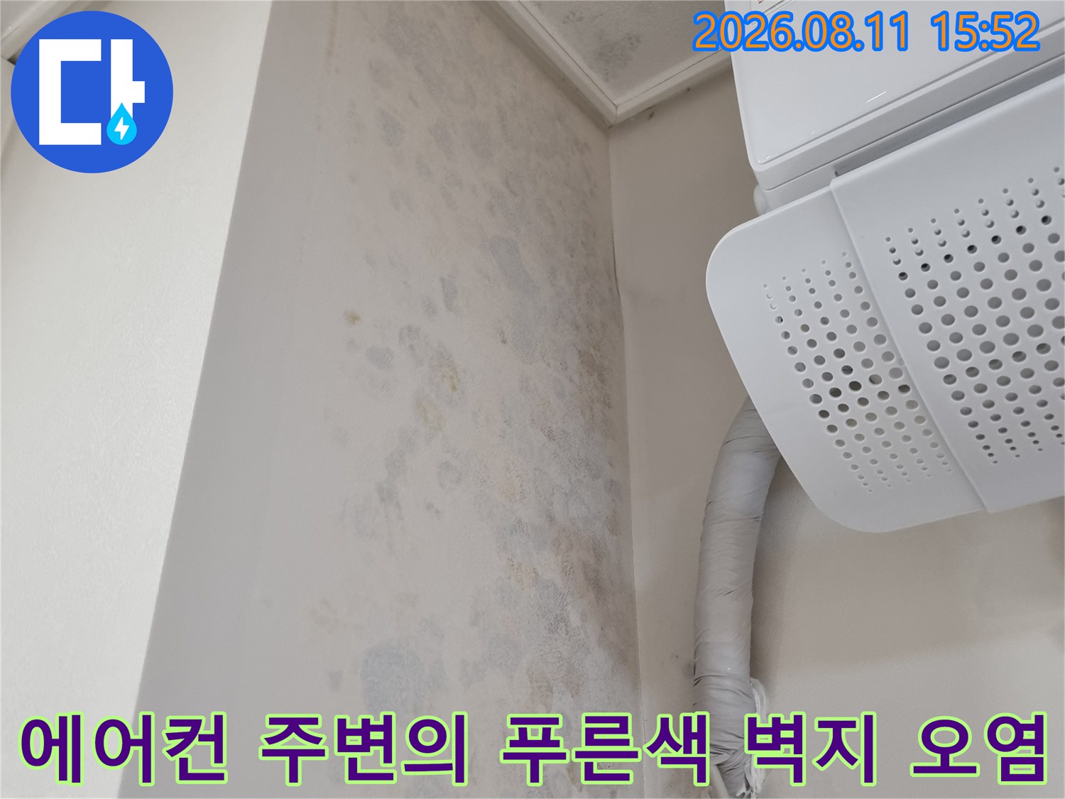 흰색 에어컨 기기와 우측 배관 그리고 그 아래로 넓게 퍼진 곰팡이 얼룩이 있는 천장 모습