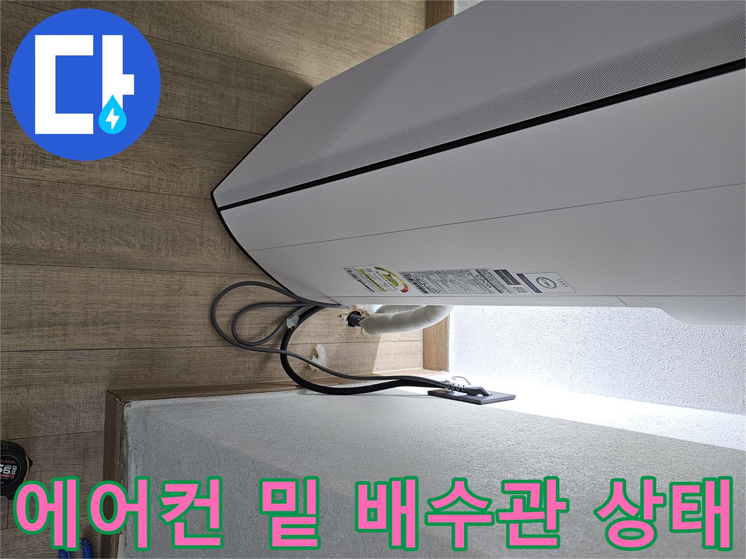 벽면과 에어컨 본체 사이의 배수 호스 연결 부위를 촬영한 이미지입니다.