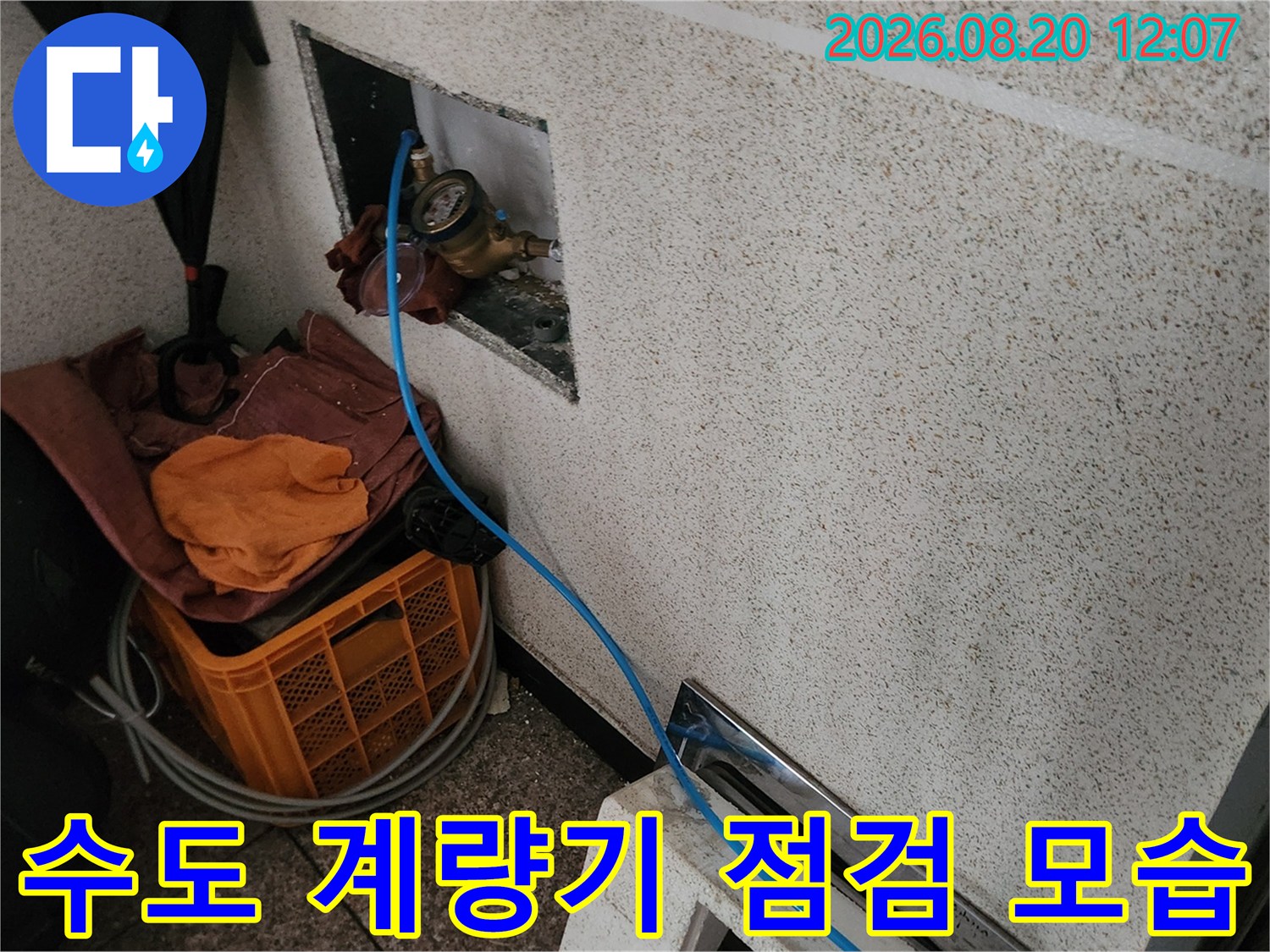 벽면 함체 내부의 수도 계량기와 점검용 파란색 호스