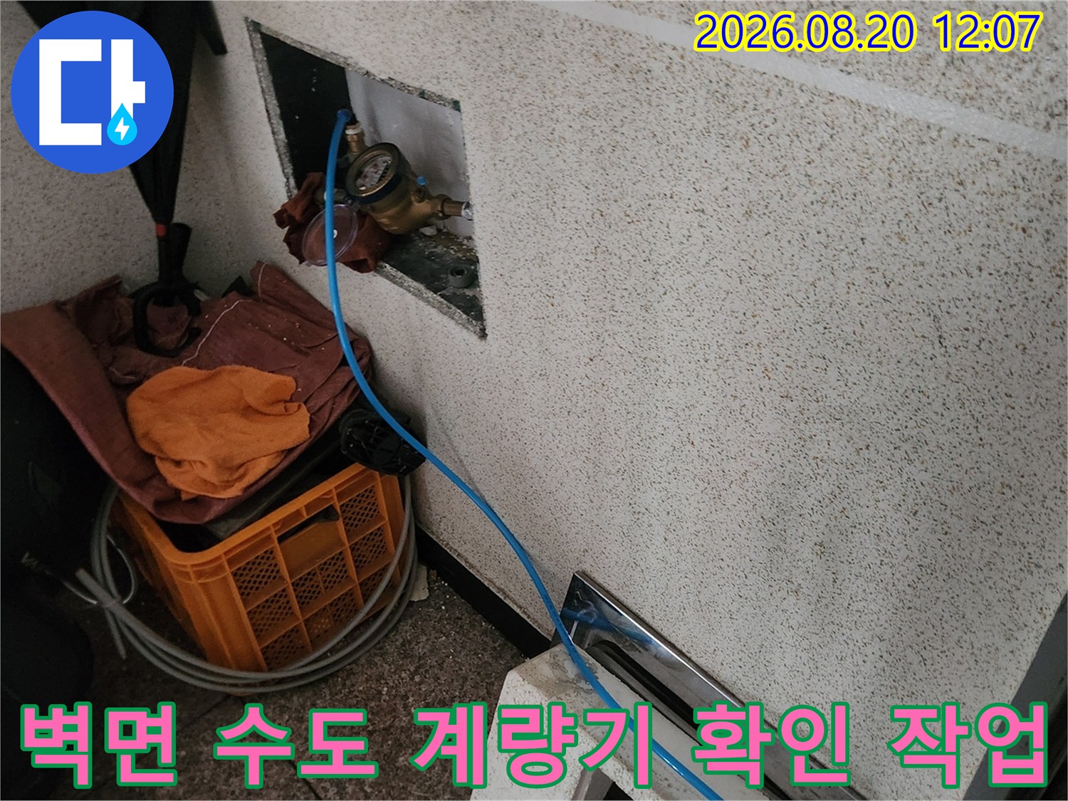 타일 벽 안쪽 공간에 설치된 수도 계량기와 배관의 모습입니다.