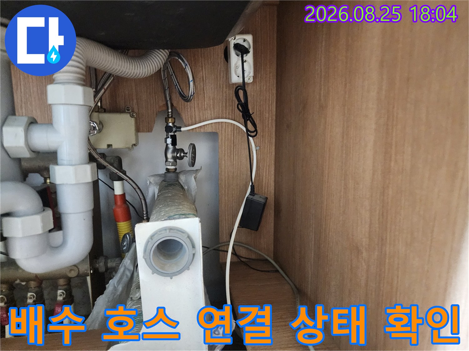 하얀색 주름관 배수 호스와 금속 재질의 급수 밸브가 연결된 싱크대 하단 모습입니다.