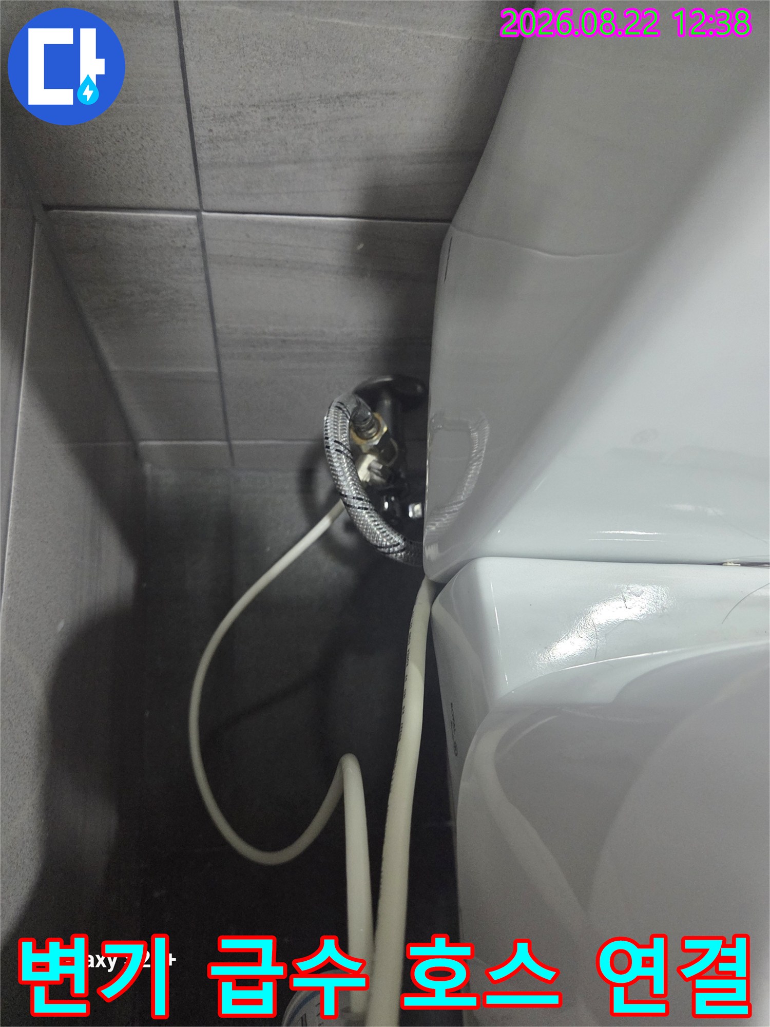벽면 타일과 변기 탱크를 잇는 급수 밸브와 유연한 호스 모습입니다.