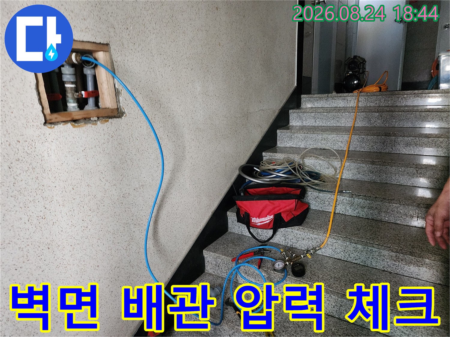 파란색 호스가 연결된 벽체 노출 배관과 측정 장비의 모습