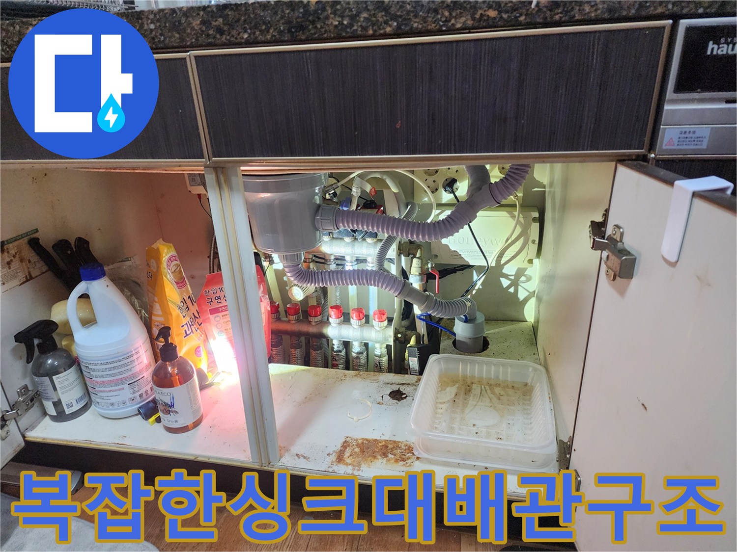 싱크대 하부장의 복잡하게 얽힌 배수 배관과 에어컨 호스 연결부