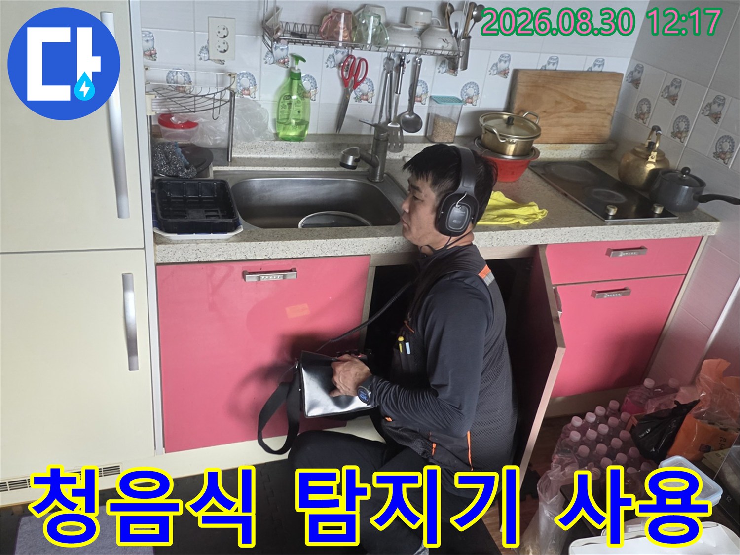 싱크대 하단에서 청음식 탐지기를 사용하여 누수 지점을 찾는 모습입니다.