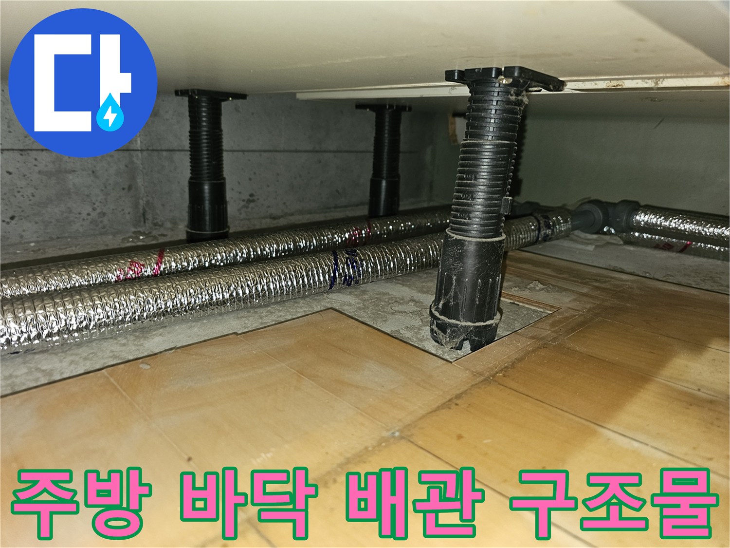 싱크대 하단 공간의 검은색 지지대와 은박 보온재로 감긴 배관 모습