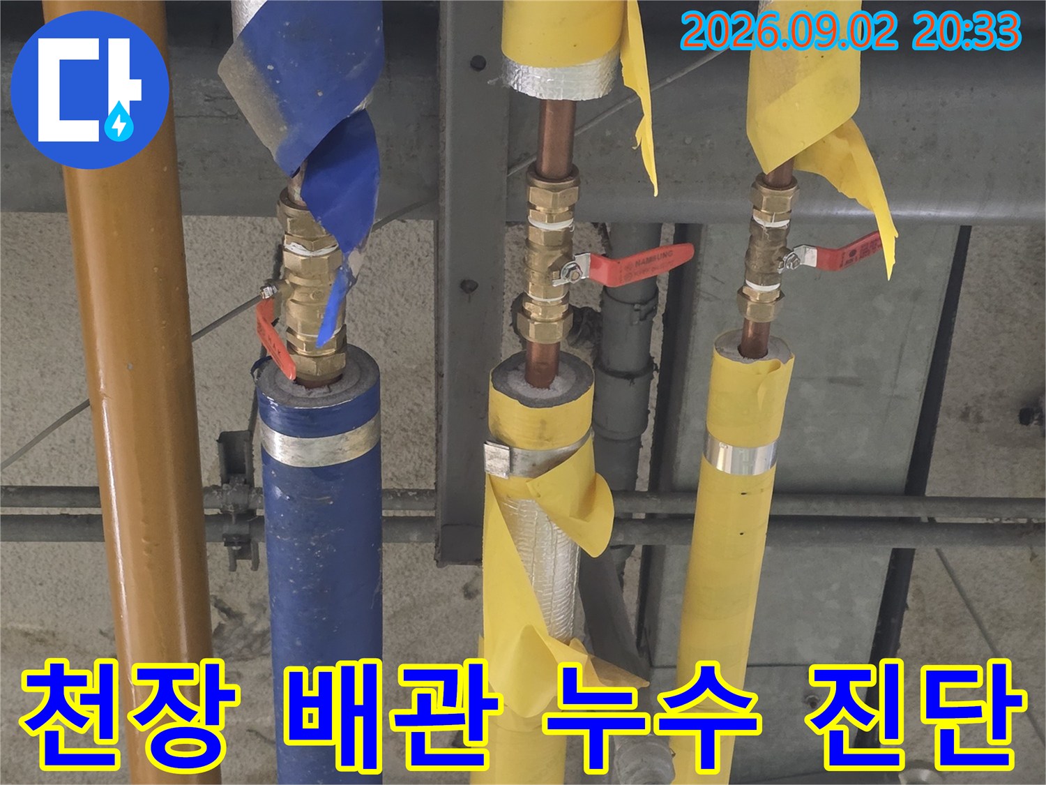노란색-및 파란색 보온재가 씌워진 천장 배관의 연결 부위 점검 모습입니다.