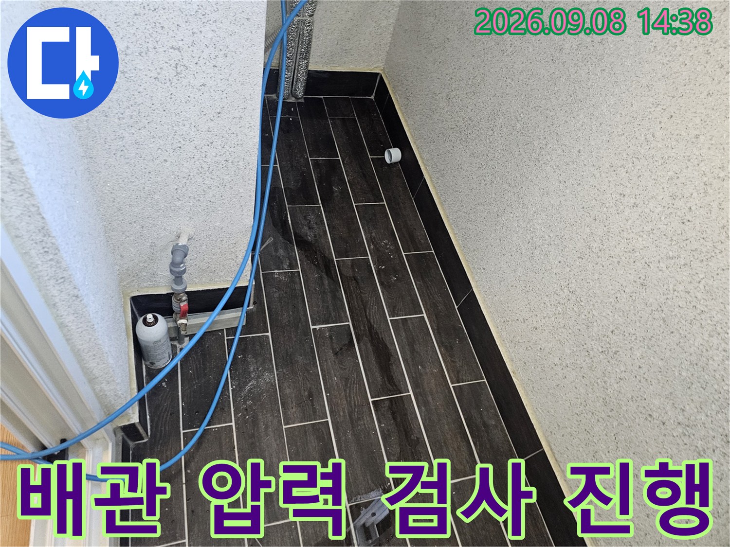 어두운 색 타일 벽면 옆에서-파란색 호스를 연결하여-배관 압력 검사를 수행하는 모습입니다.