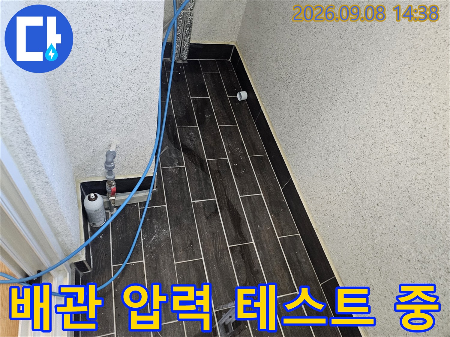파란색 호스가 연결된 어두운 색상의 타일 벽면 점검 부위