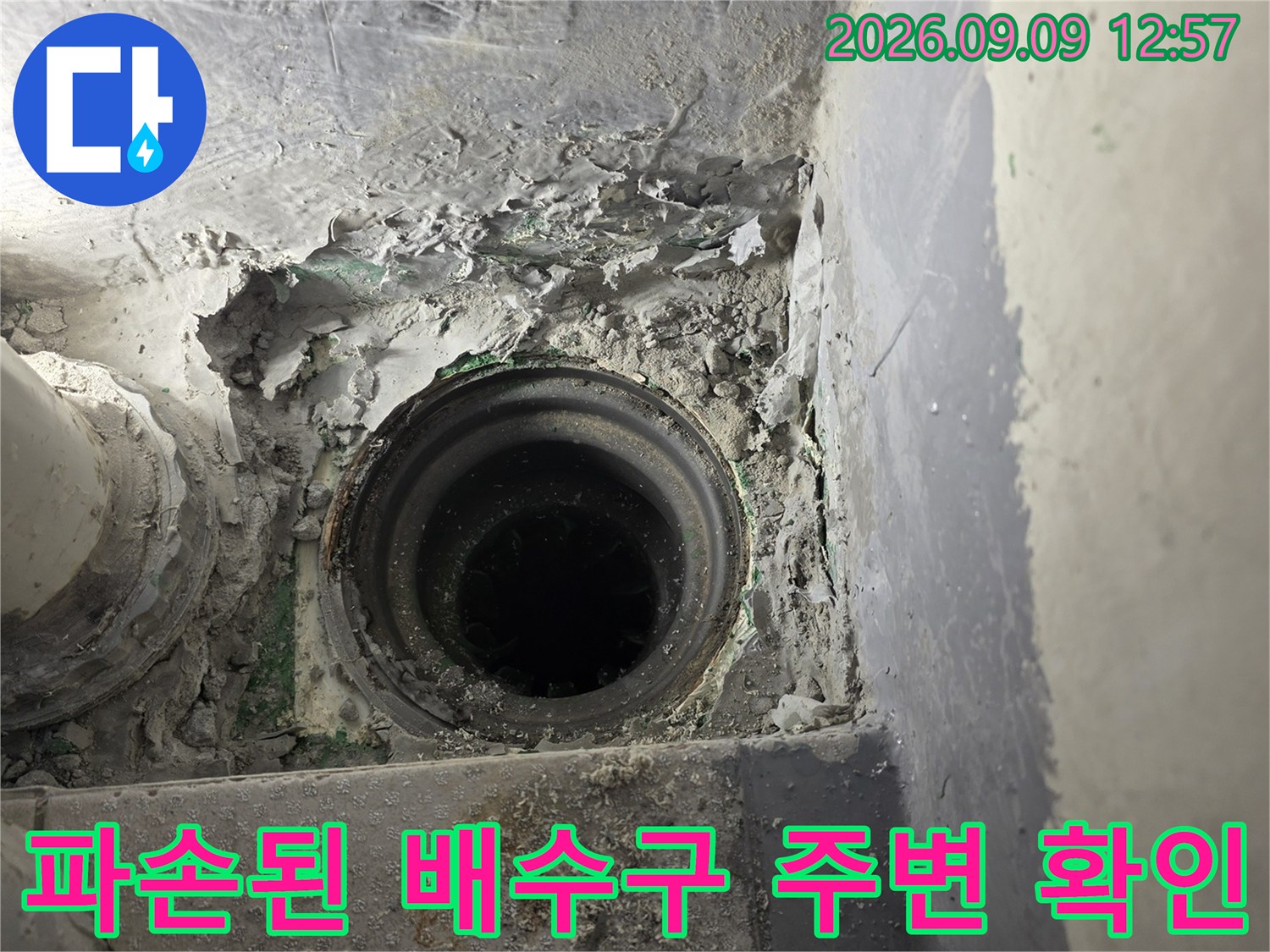 배수구 주변의 깨진 시멘트와 노출된 하수관 내부