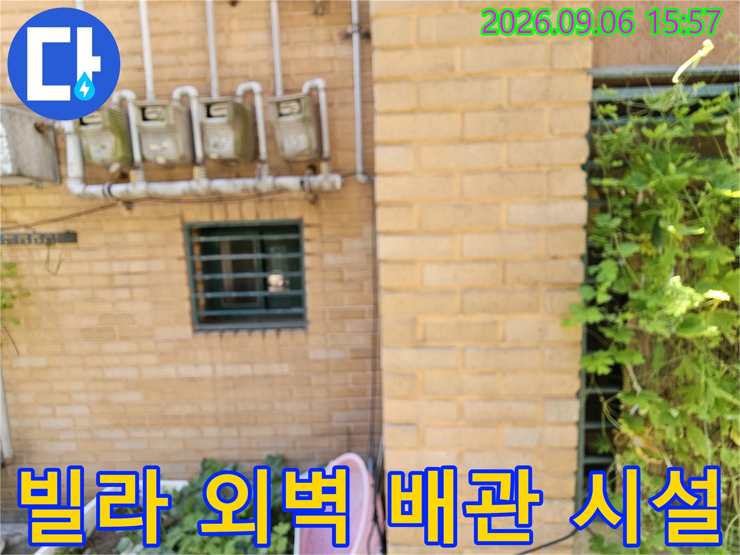 황토색 벽돌로 된 외벽에 설치된 수도 계량기와 상단 연결 관