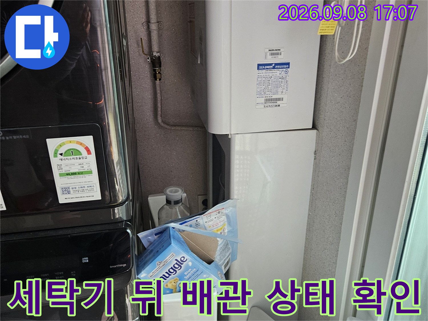 세탁기 하단부의 수도 연결 배관과 주변 구조물을 촬영한 사진입니다.