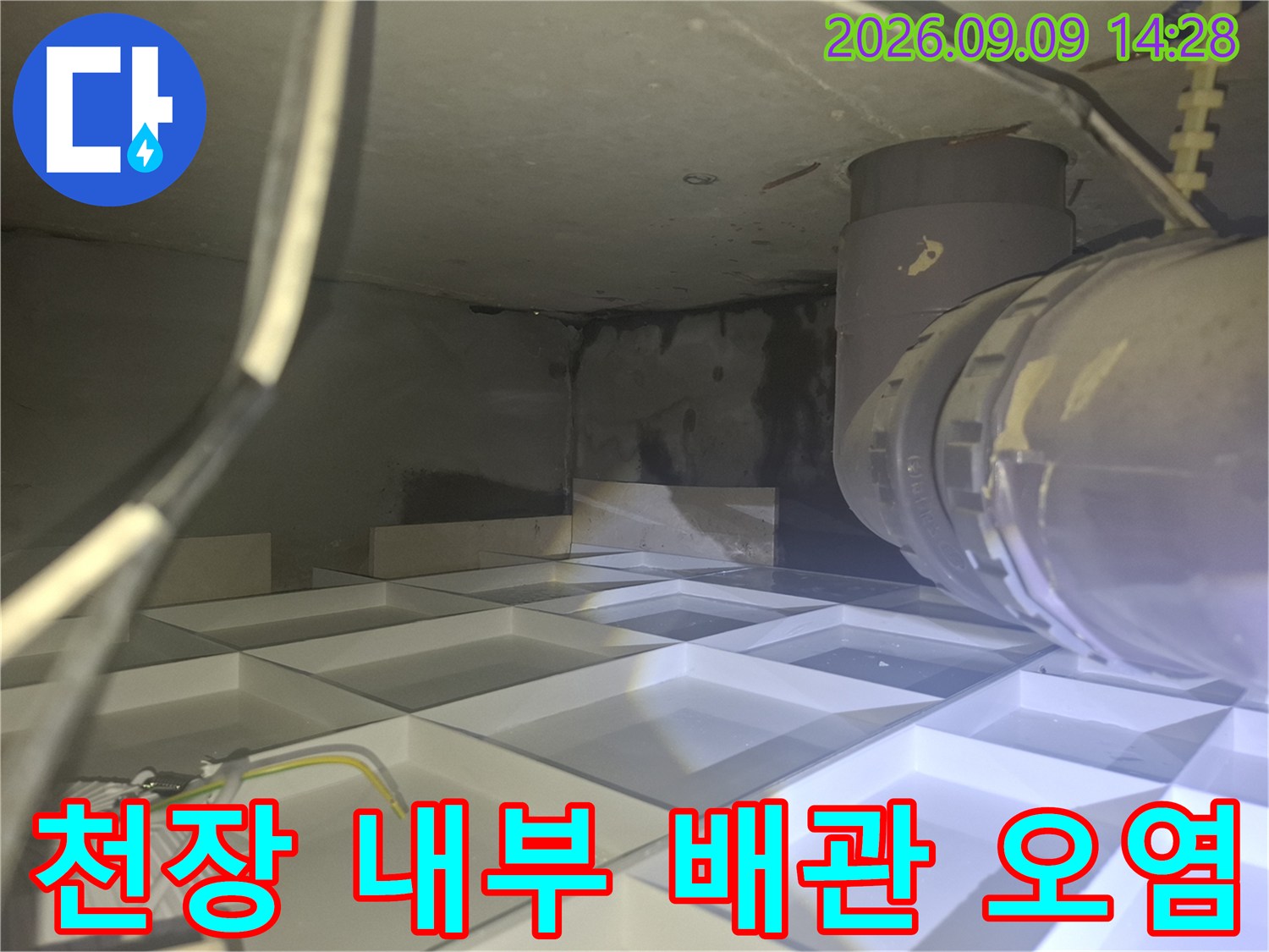 천장 마감재 안쪽의 배관과 습기로 인한 어두운 얼룩 상태를 보여줍니다.