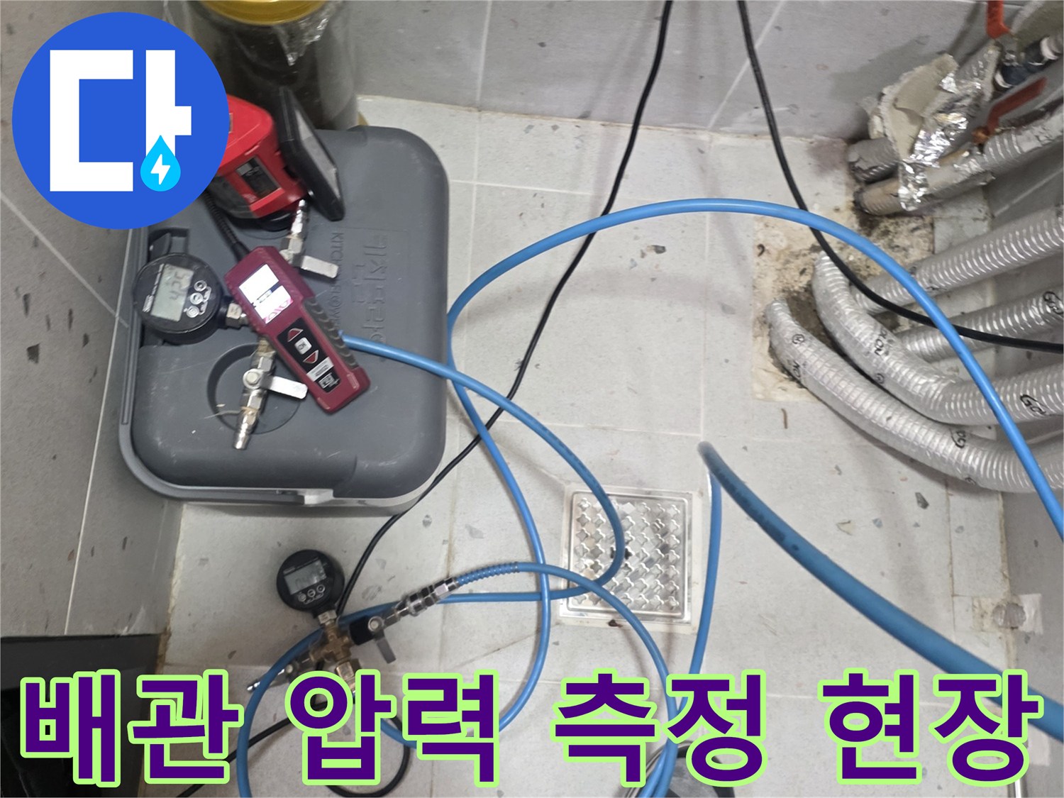 바닥 타일 근처 배관에 연결된 누수 탐지용 가스 장비와 호스