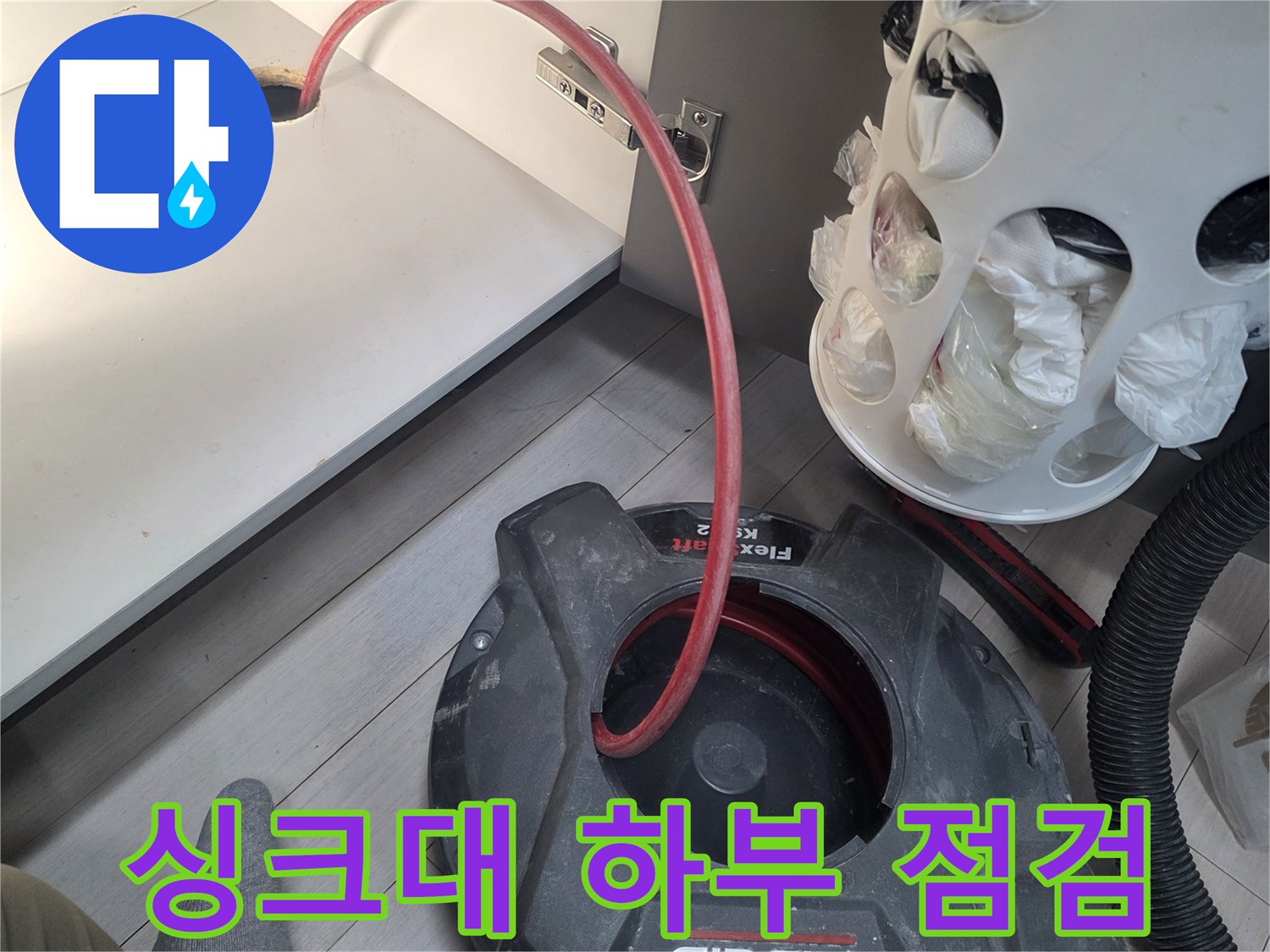 붉은 호스가 연결된 싱크대 하부장 내부의 작업 모습입니다.